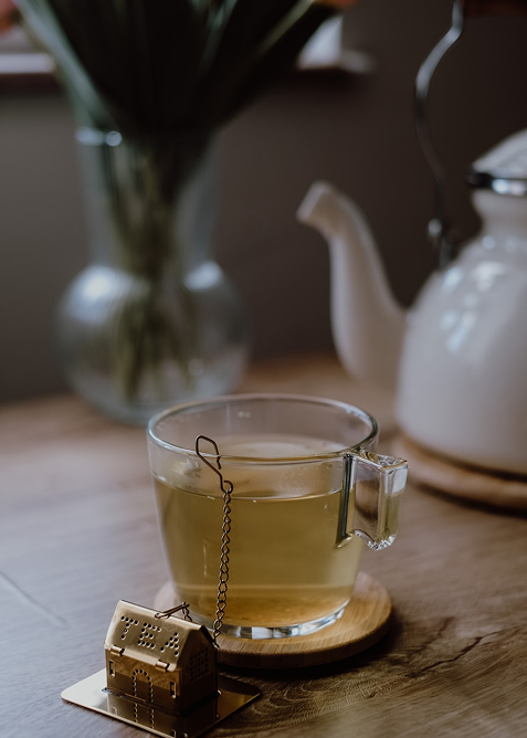Glass cup of tea with teapot nearby.